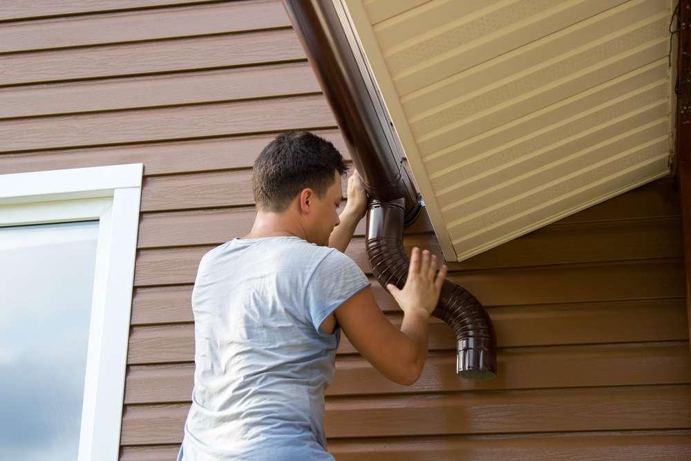 man-attaches-gutter-on-roof-porch