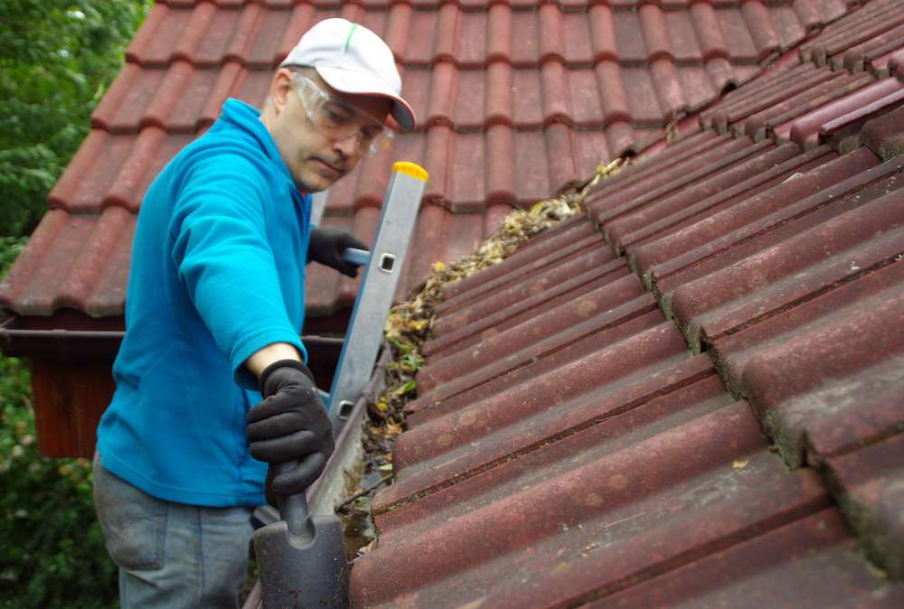 man-on-ladder-cleans-gutter-roof