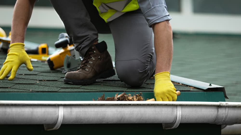 man-worker-cleaning-clogged-roof-gutter