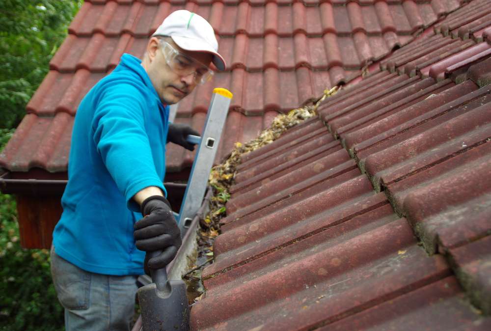 man-on-ladder-cleans-gutter-roof 